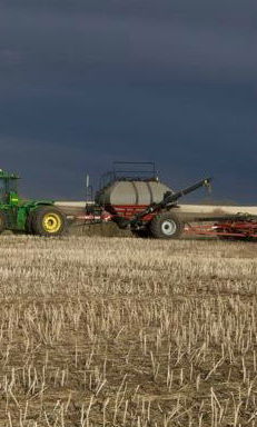 farm tractor seeding under storm clouds